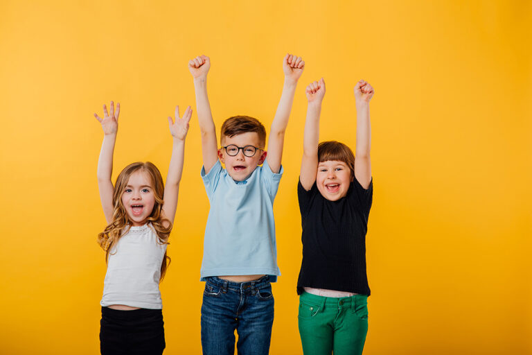 Three kids cheering with their hands in the air in front of a yellow background.
