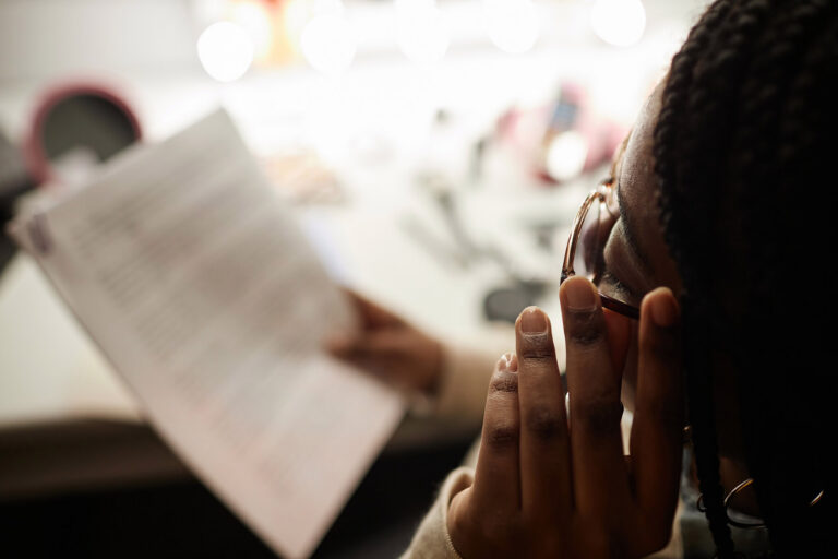 An actor reads script pages backstage by the mirror lights, memorizing lines before going on