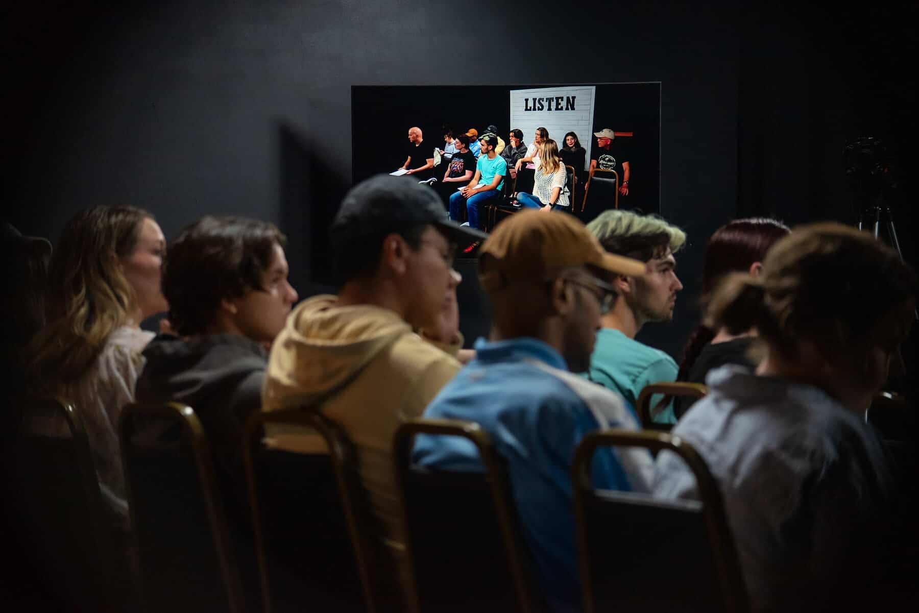 The room at Dearing Acting Studio in Phoenix from the back row, every seat taken, a scene on the far stage under the LISTEN sign