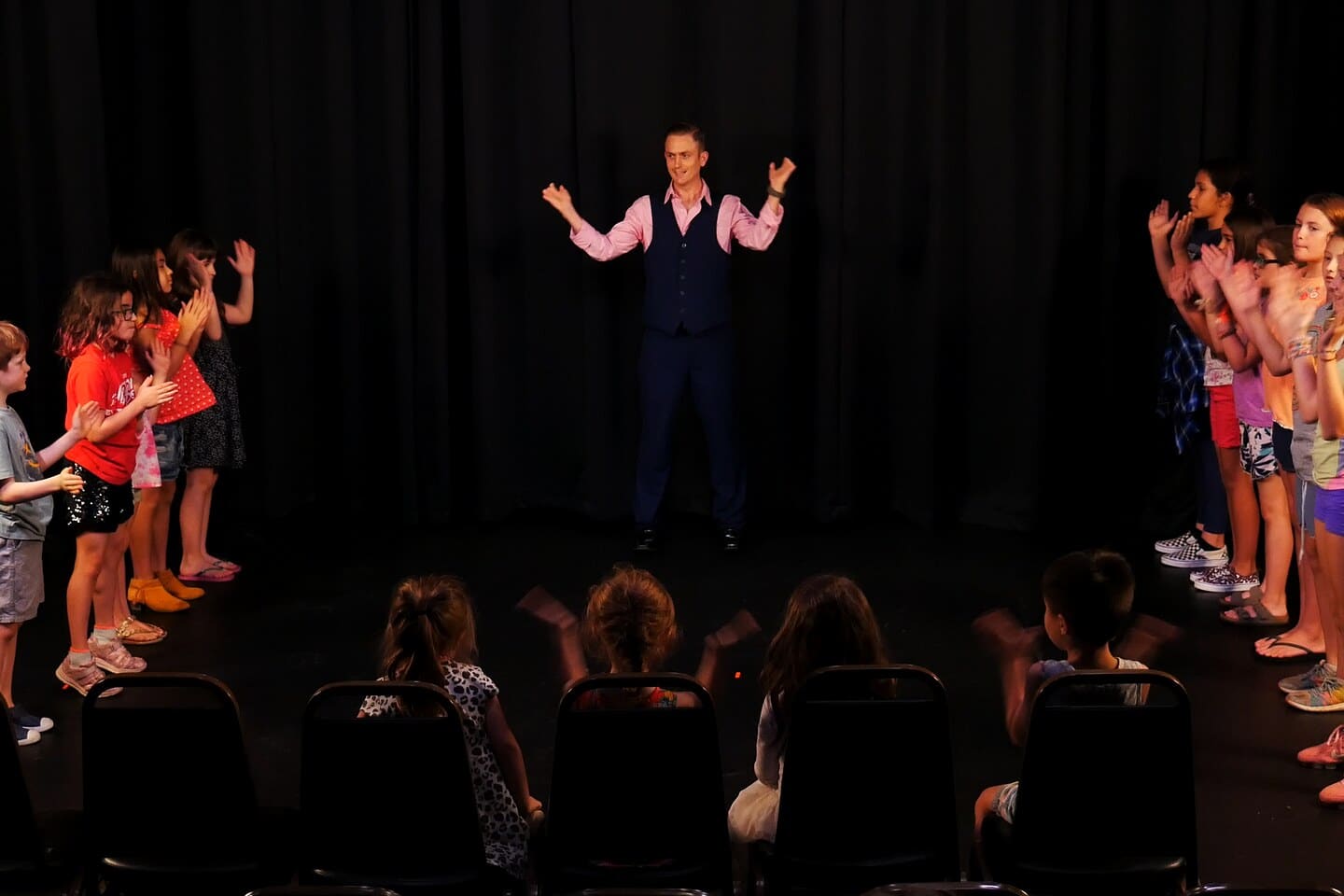 A full kid improv class standing in a ring on the lit stage at Dearing Acting Studio